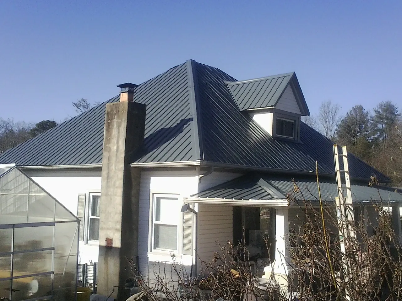 Dark blue standing seam metal roof on a white farmhouse with dormer — Slate & Tile Roof Repair by Roofing Brothers in Cato