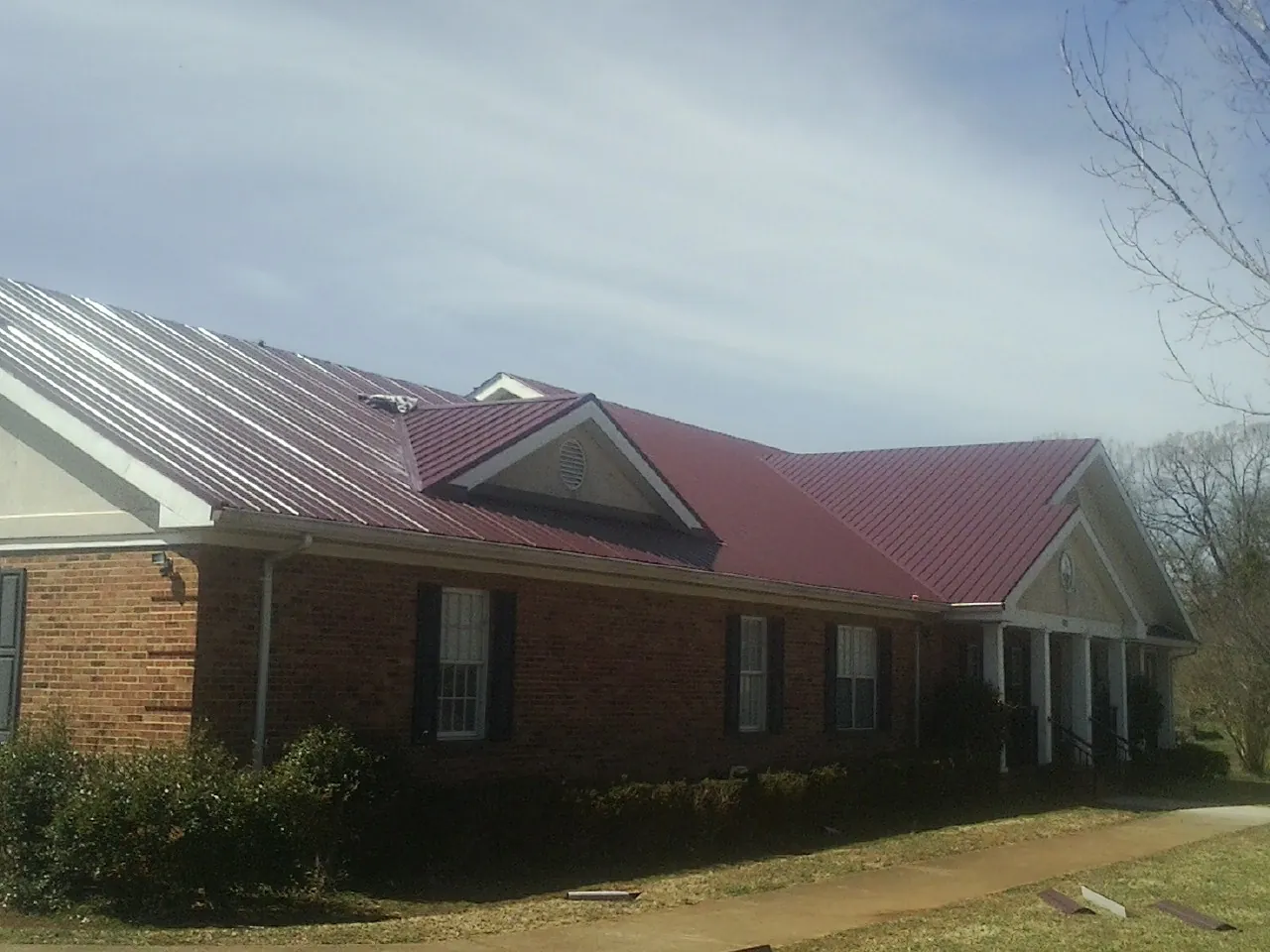 Red metal roof with gabled entries on a long brick building, from a Hail Damage Roof Repair job in Cato