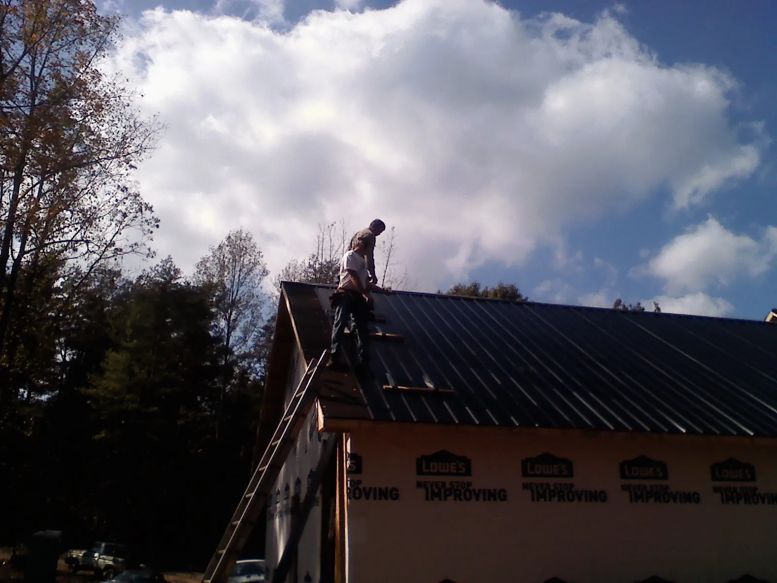 Roofer fastening dark metal panels high against a cloudy sky, from a Roof Inspection job in Cato