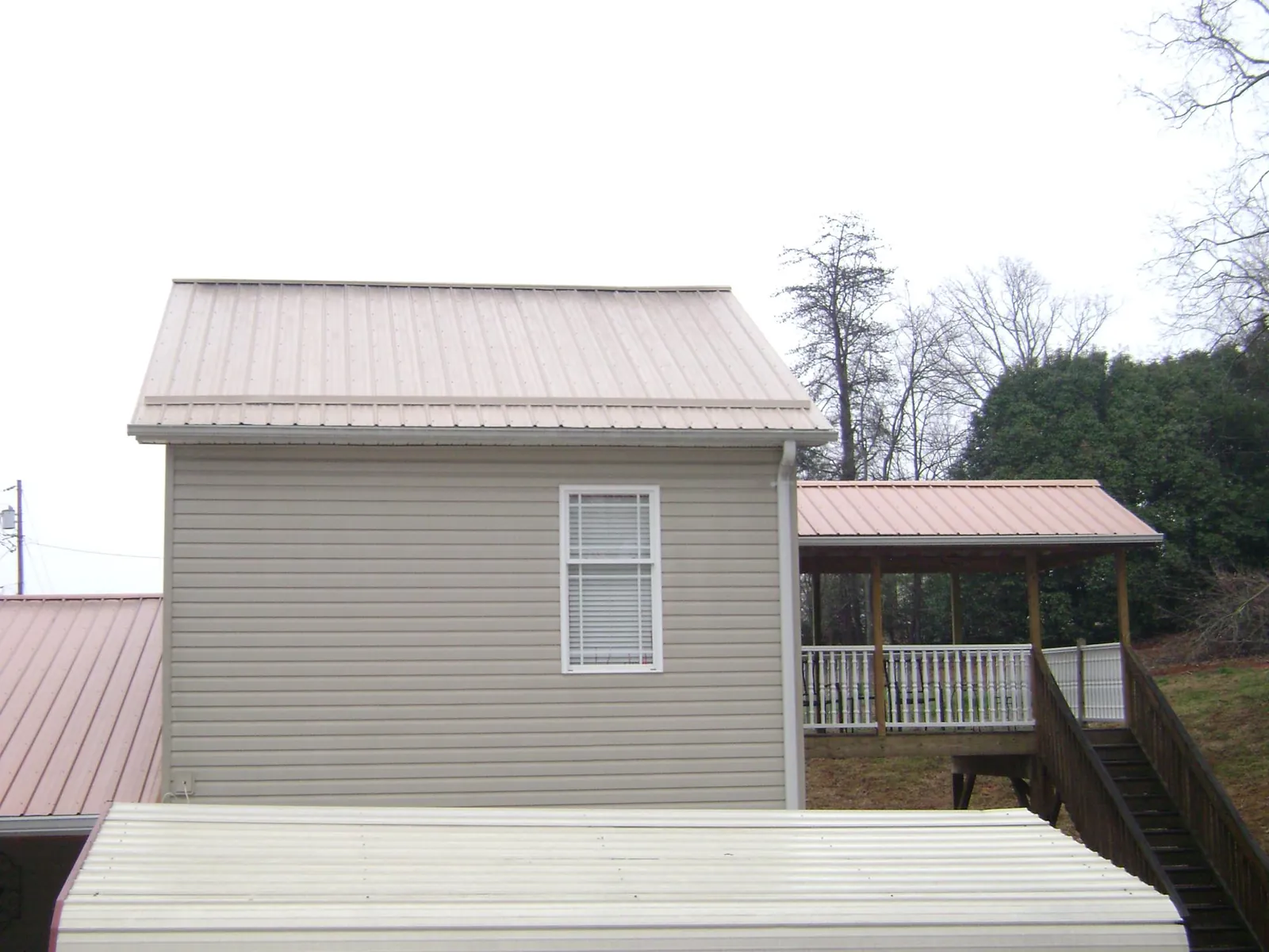 Tan metal roofs on a two story addition and attached porch, from a Roof Replacement job in Cato